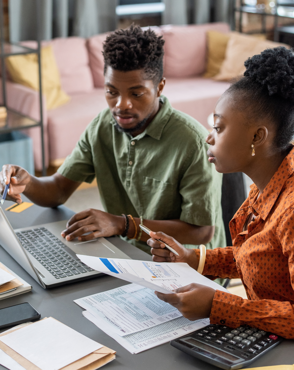 man and woman sitting at computer with stack of papers and calculator