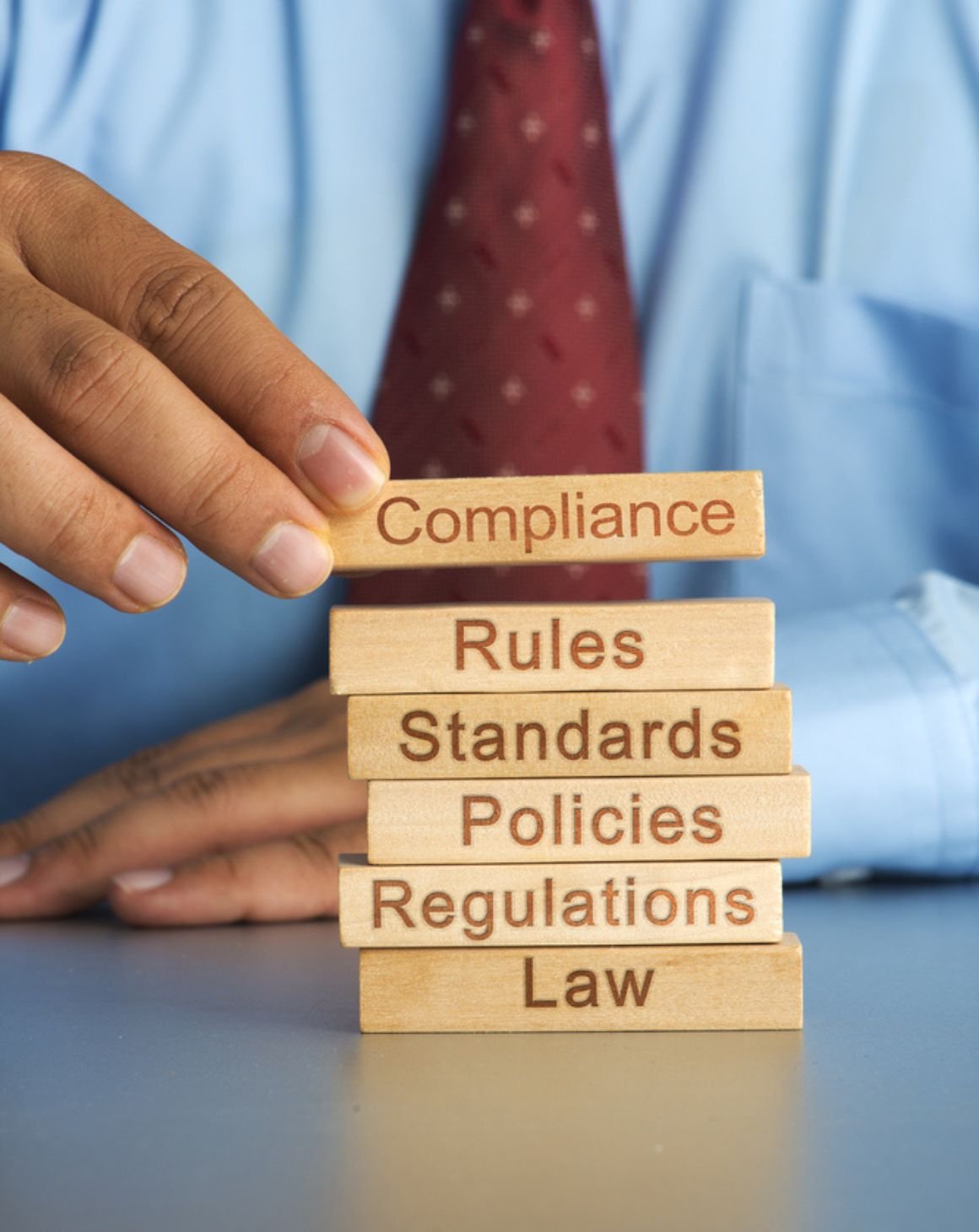 a man stacking blocks that say "compliance, rules, standards, policies, regulations, law"