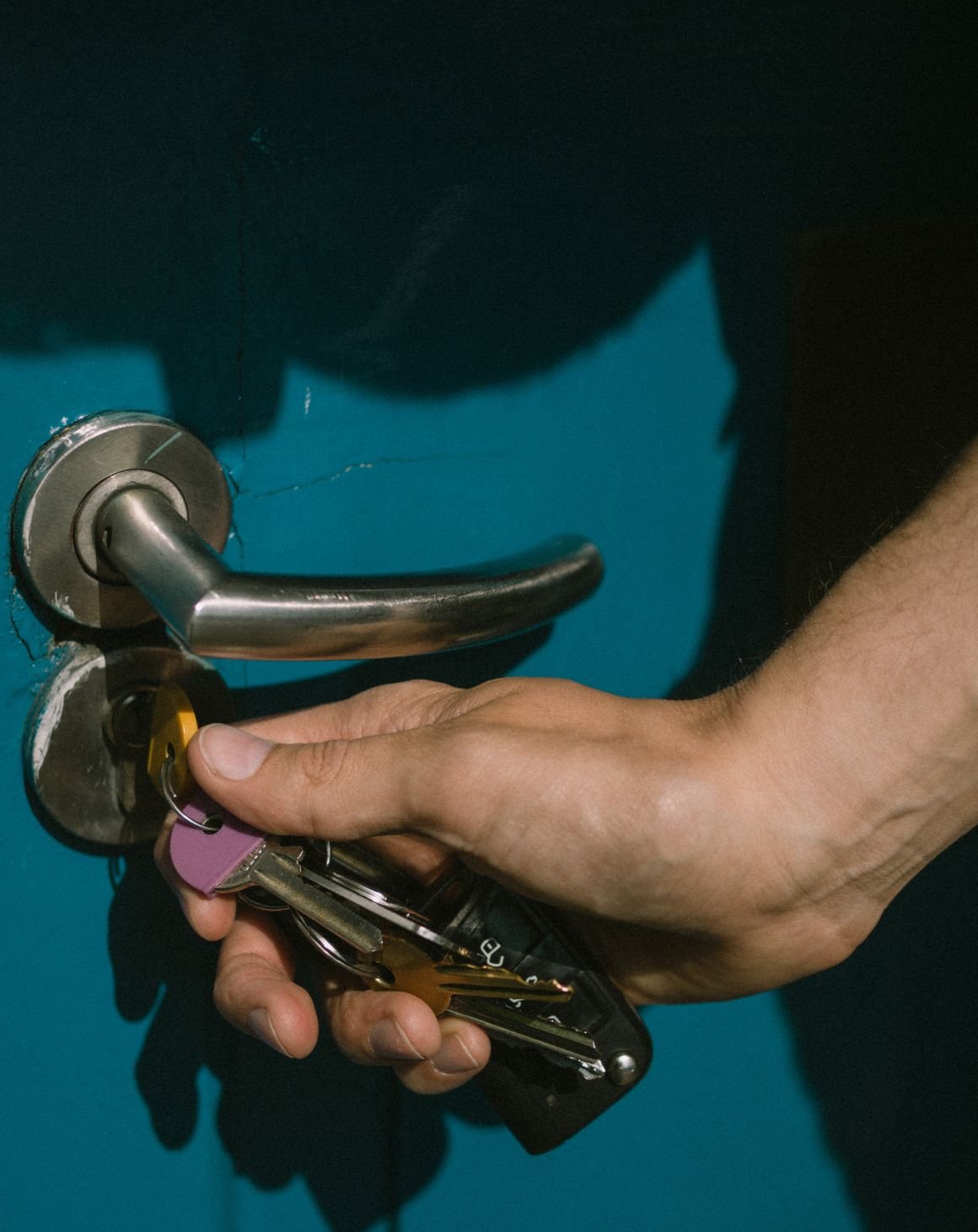 A hand unlocking a blue door with a set of keys