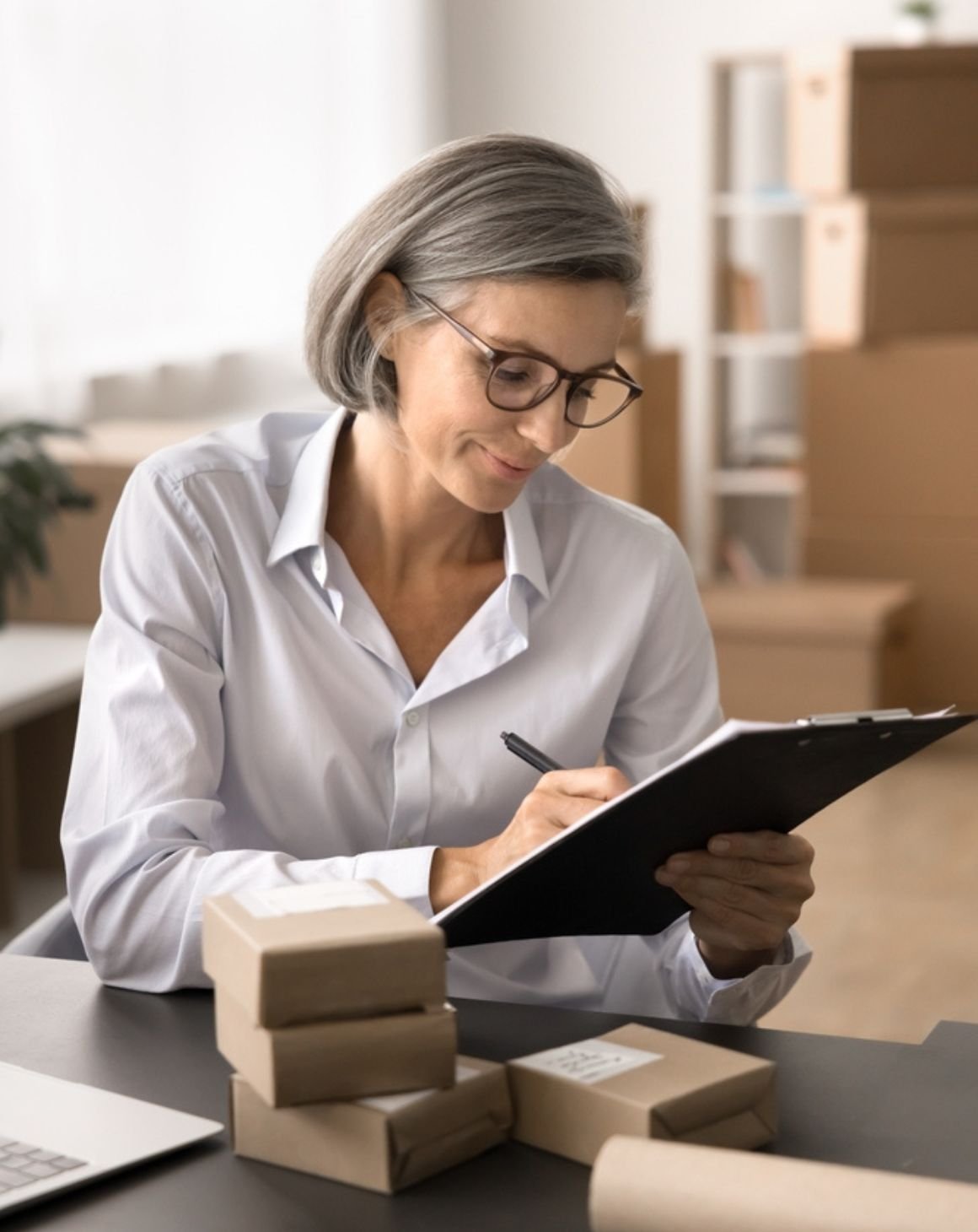 a woman wearing glasses writes notes on a clipboard