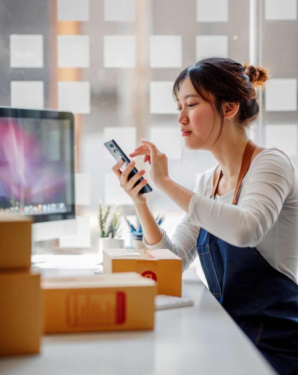 a woman sitting at a desk, focused on her phone, surrounded by a tidy workspace