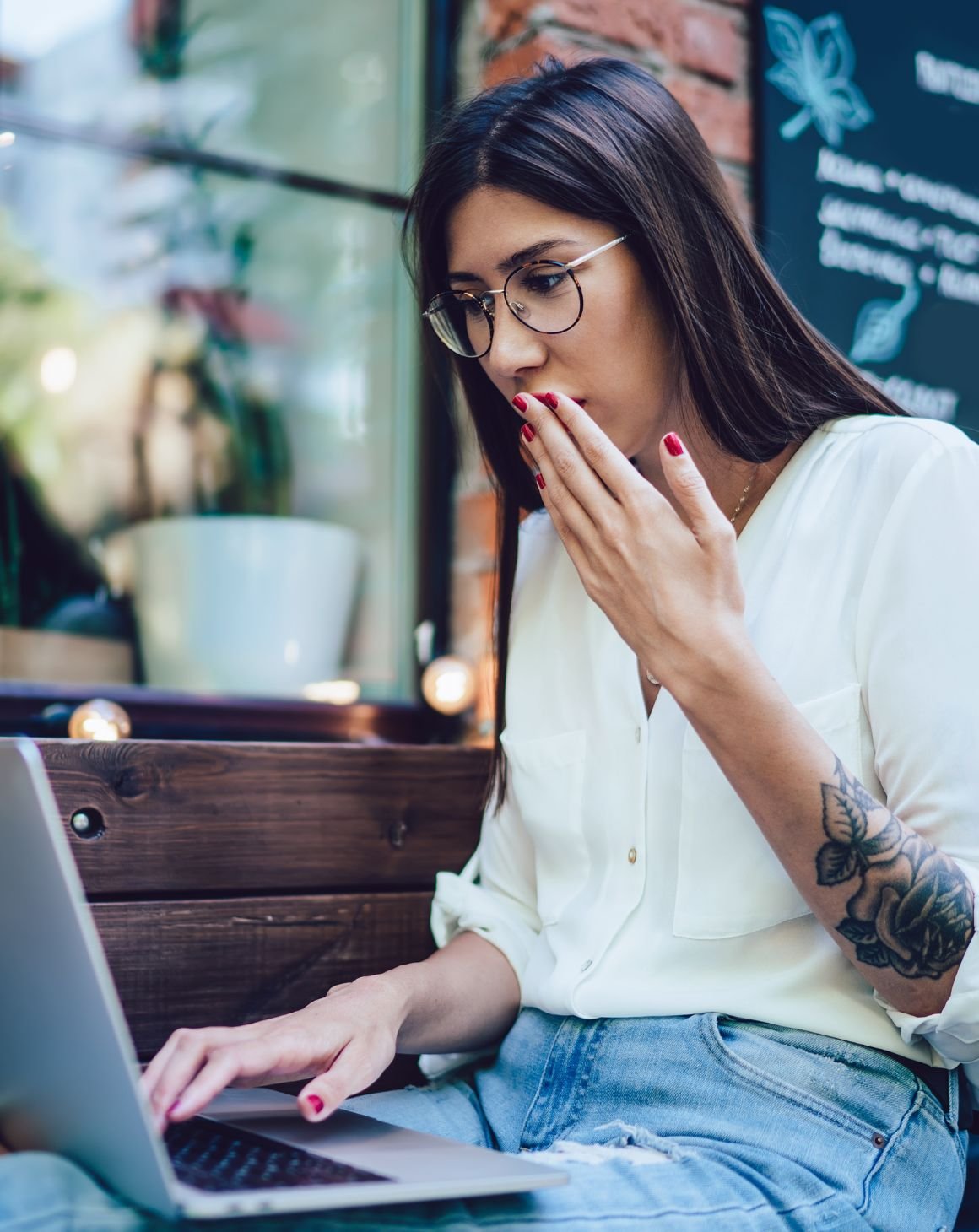 surprised woman sitting outside a café using a laptop