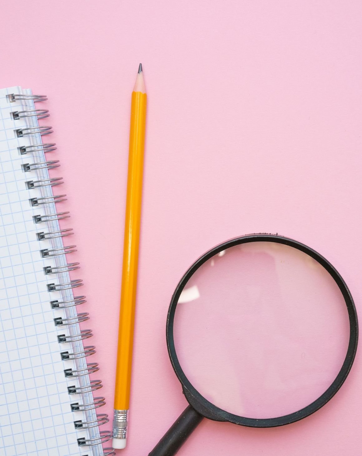 A magnifying glass, a pencil, and a notebook for performing amazon keyword research