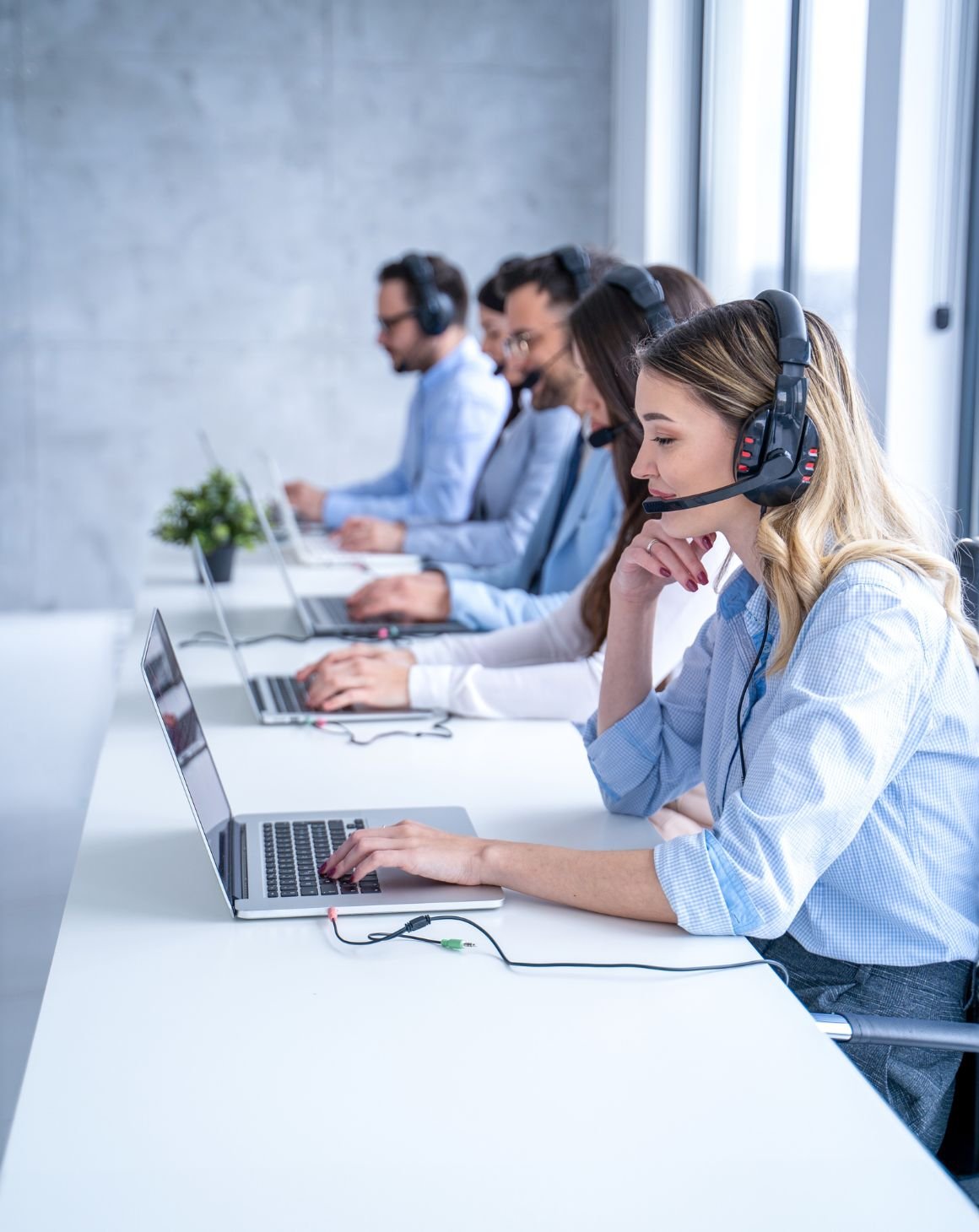 group of employees on laptops at a desk with headphones